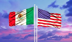 Mexican and American flag wave over a sunset